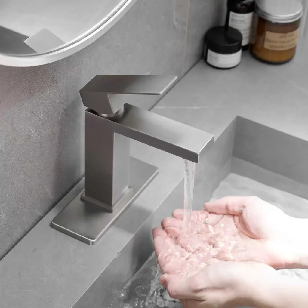 Silver square bathroom faucet with running water installed on a gray sink
